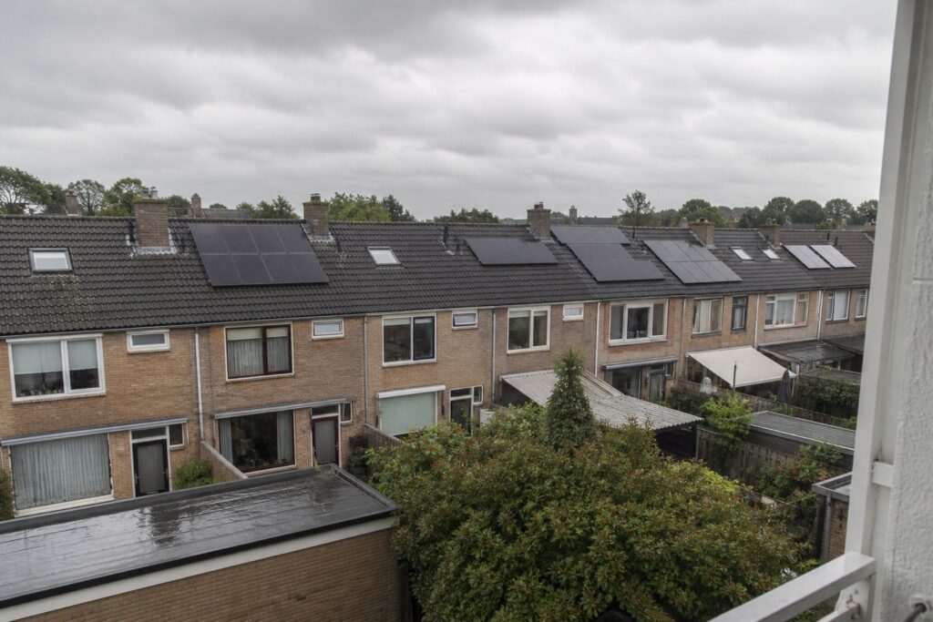 Rij rijtjeshuizen met zwarte zonnepanelen op de dakpannen onder een bewolkte lucht